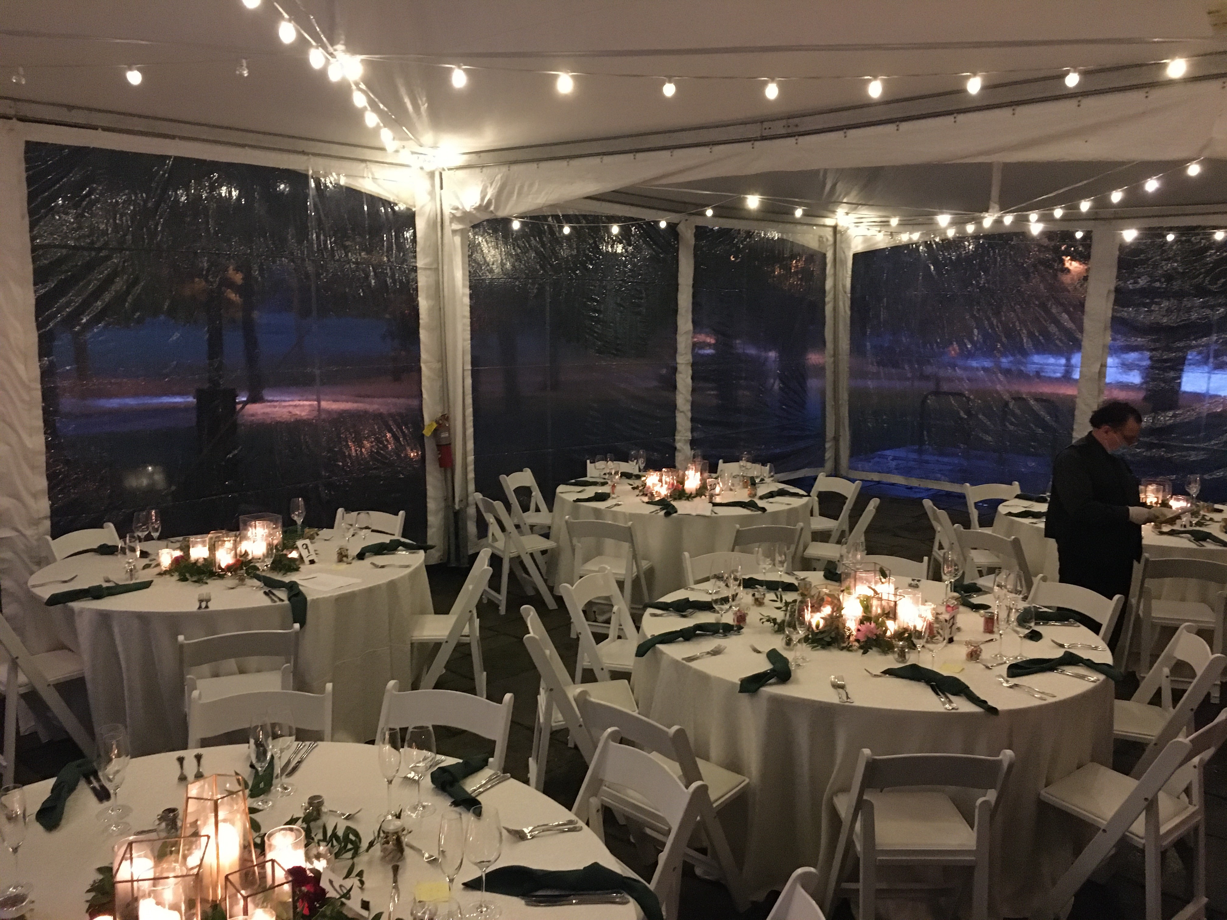 Wedding reception tent at night with white tablecloths, centerpieces, and string lights.
